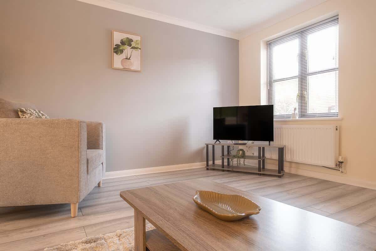 A living room with a sofa, a coffee table, a flat-screen TV on a stand, and a window with blinds.