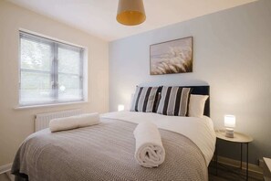 A neatly made bed with a striped pillow, a bedside lamp, and a window with blinds.