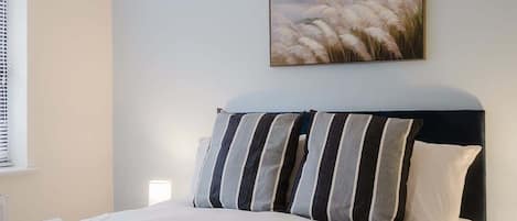 A bedroom with a bed, pillows, a wall-mounted painting, and a window with blinds.