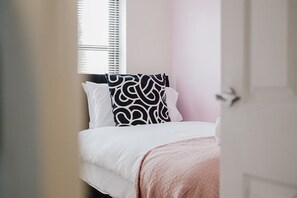 A bedroom with a bed, a window with blinds, and a door.