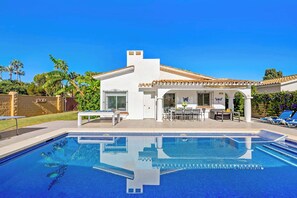 Ett modernt hus med en swimmingpool, utemöbler och en täckt uteplats.