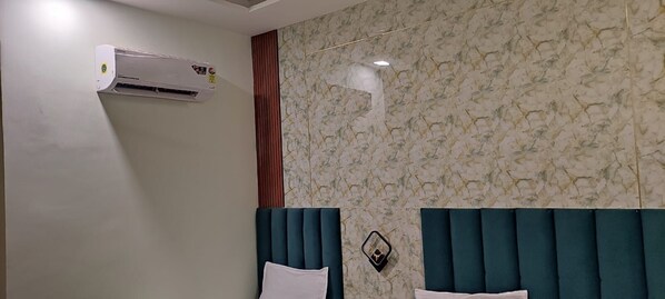 A hotel room with a marble-patterned wall, a white air conditioner, a wooden panel, a teal headboard, and a bedside table with a lamp. - Hotel Relaxx Luxury (Amritsar)
