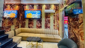 A modern lobby with a curved sofa, a flat-screen TV, marble walls, and a staircase. - Hotel Relaxx Luxury (Amritsar)