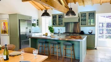 Een moderne keuken met een centraal kookeiland, barstoelen en een eethoek met een tafel voor twee personen.