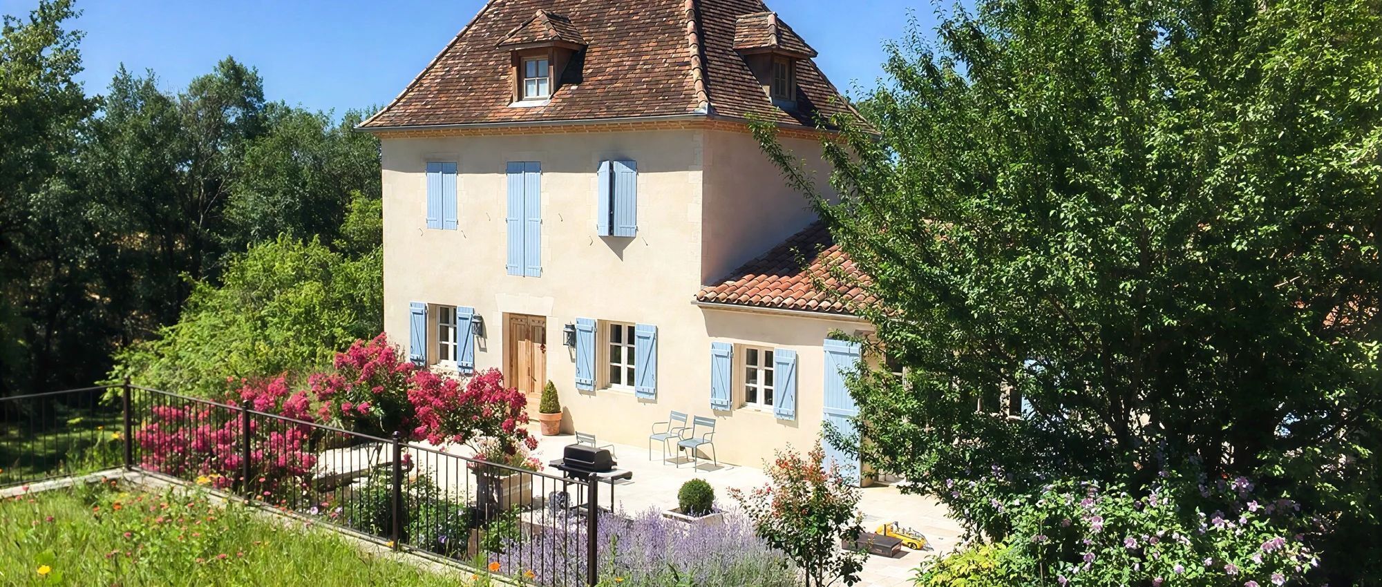 A two-story house with a tiled roof, a balcony, and a garden with various plants and flowers.