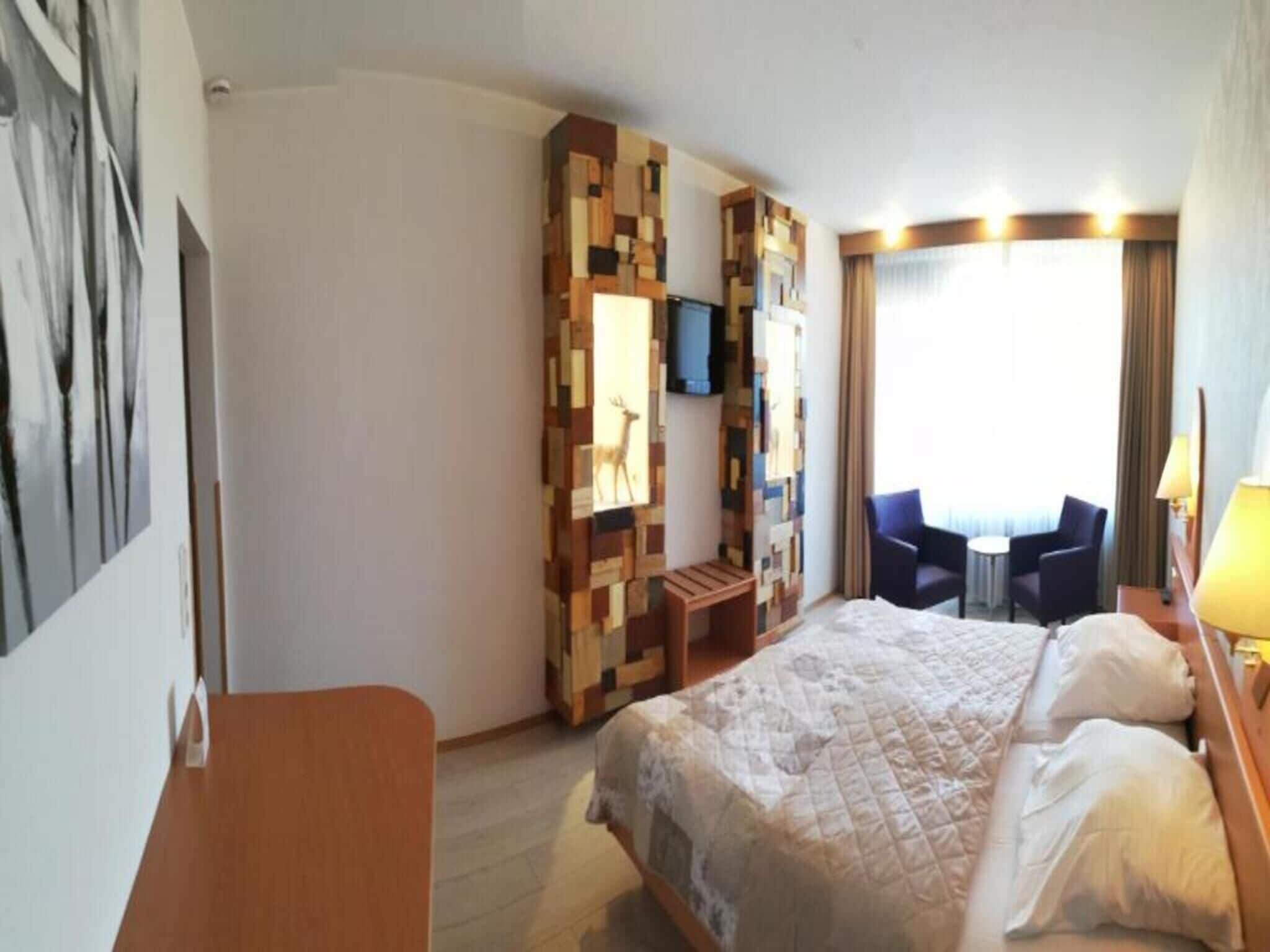 Habitación de hotel con cama, escritorio, silla, televisor y ventana con cortinas.