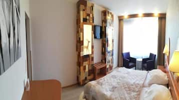 Habitación de hotel con cama, escritorio, silla, televisor y ventana con cortinas.