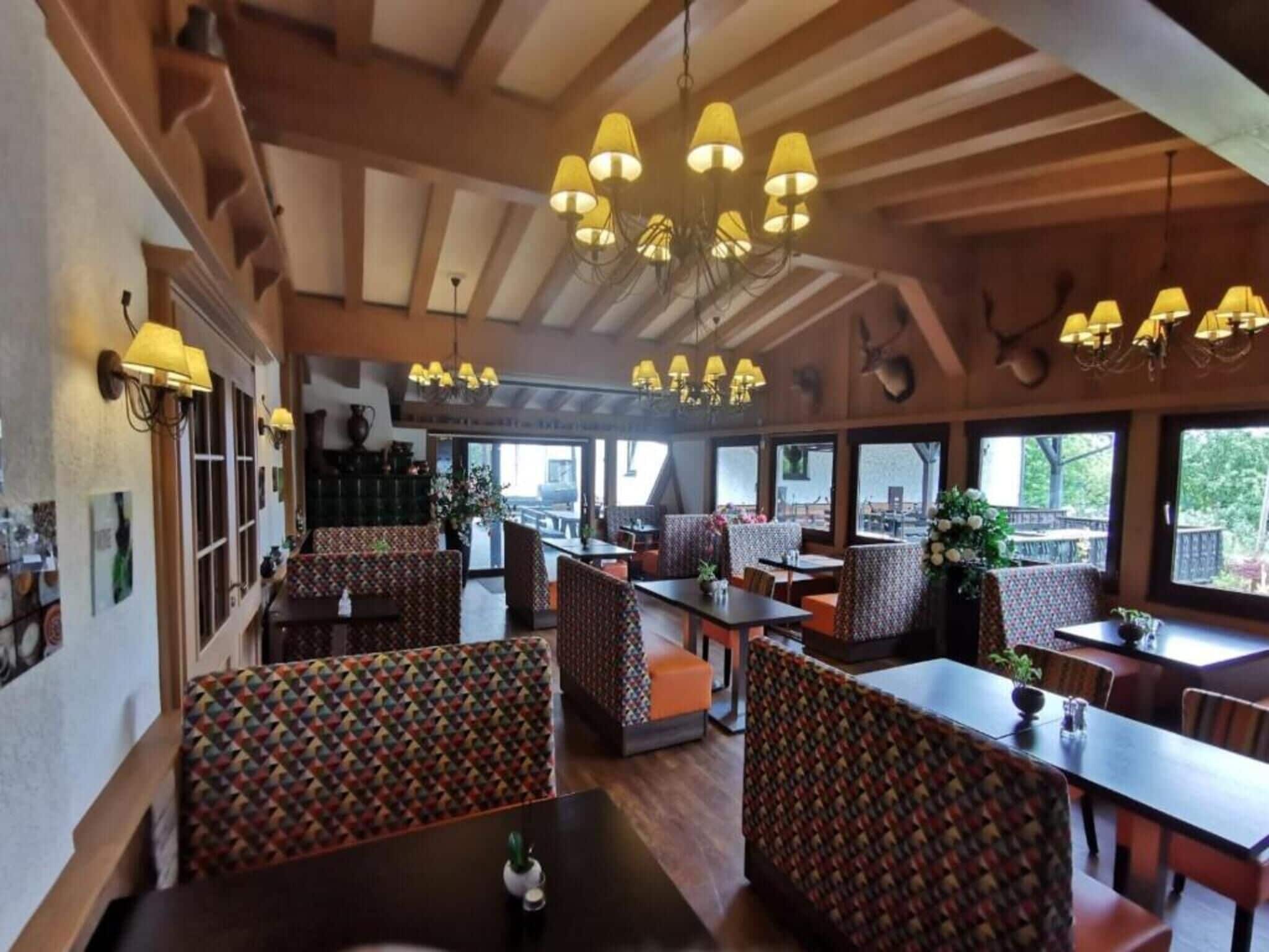 A restaurant with wooden beams, patterned booths, and hanging lamps.