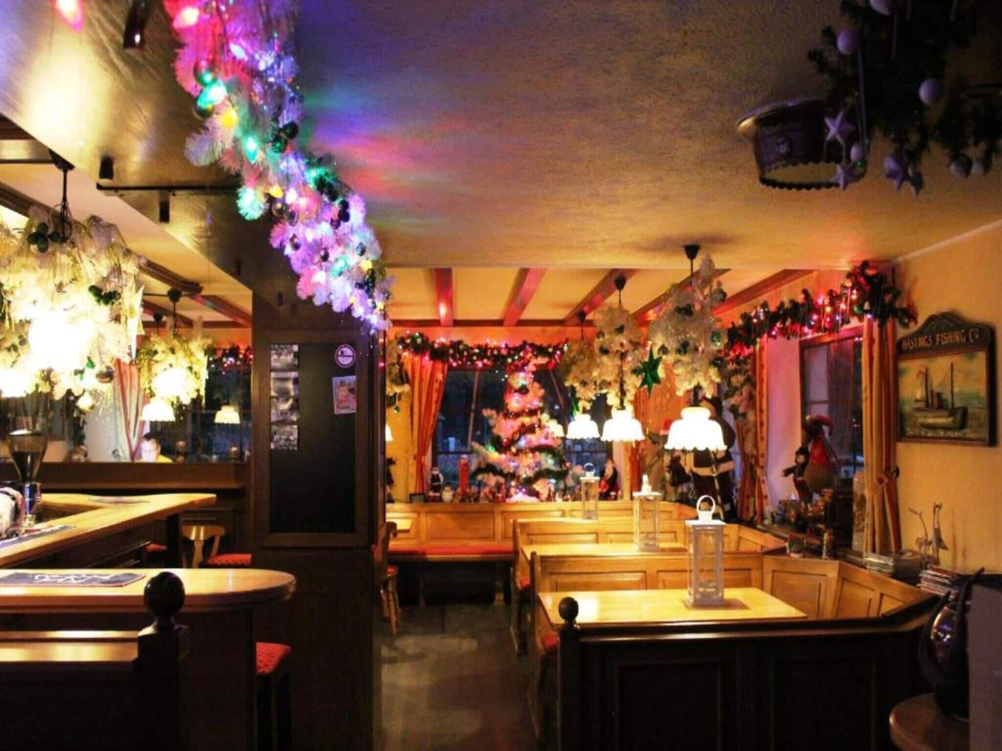 Ein Restaurantinneres mit Holztischen und -stühlen, hängenden Blumendekorationen und einem weihnachtlichen Hintergrund.