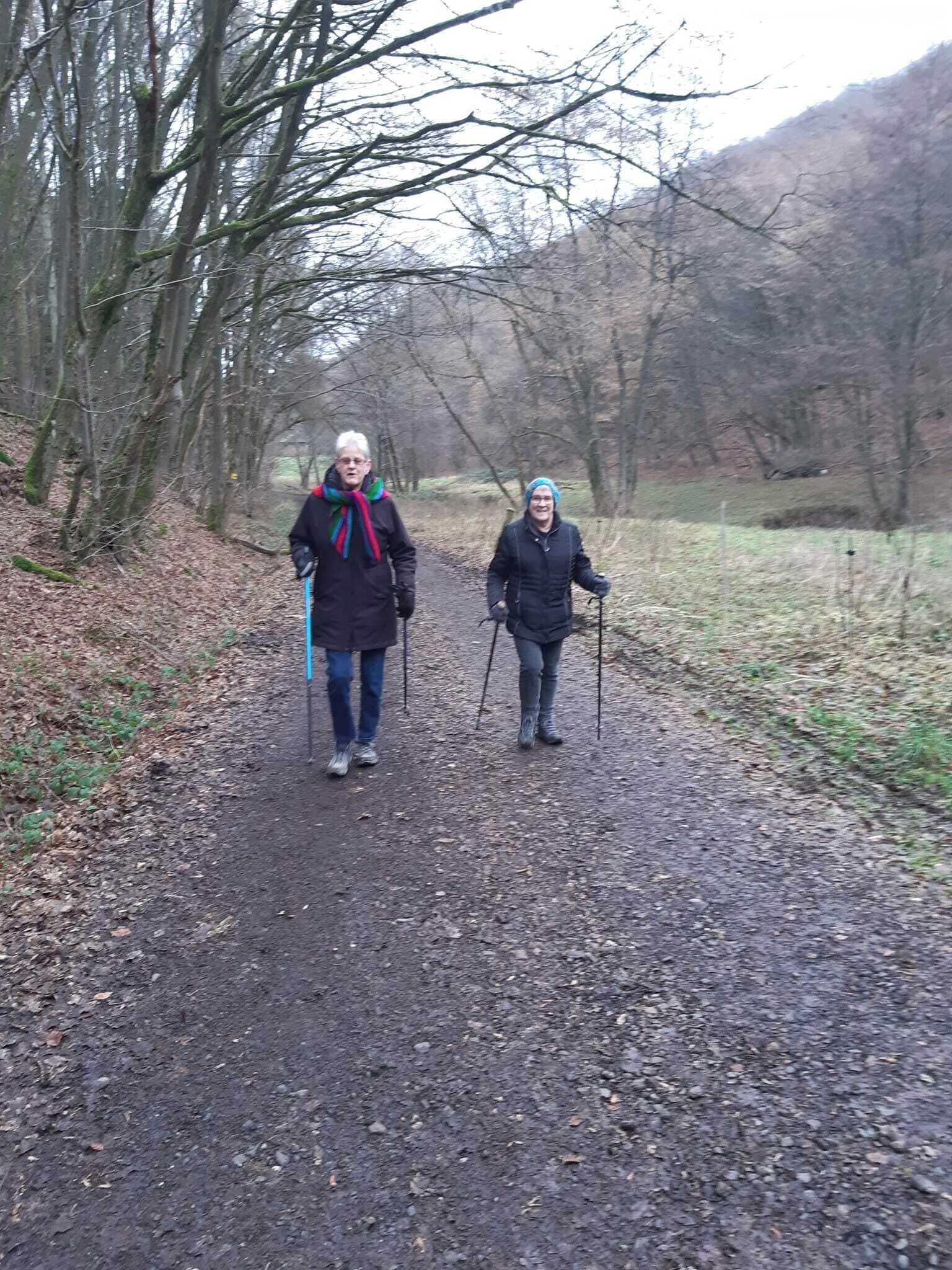 Dos personas caminando por un sendero de tierra rodeado de árboles.