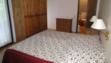Ein Schlafzimmer mit einem Bett, einem Holzschrank, einer kleinen Kommode und einer Lampe.