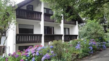 Un immeuble à plusieurs étages doté de balcons, entouré d’une végétation luxuriante et de plantes en fleurs.