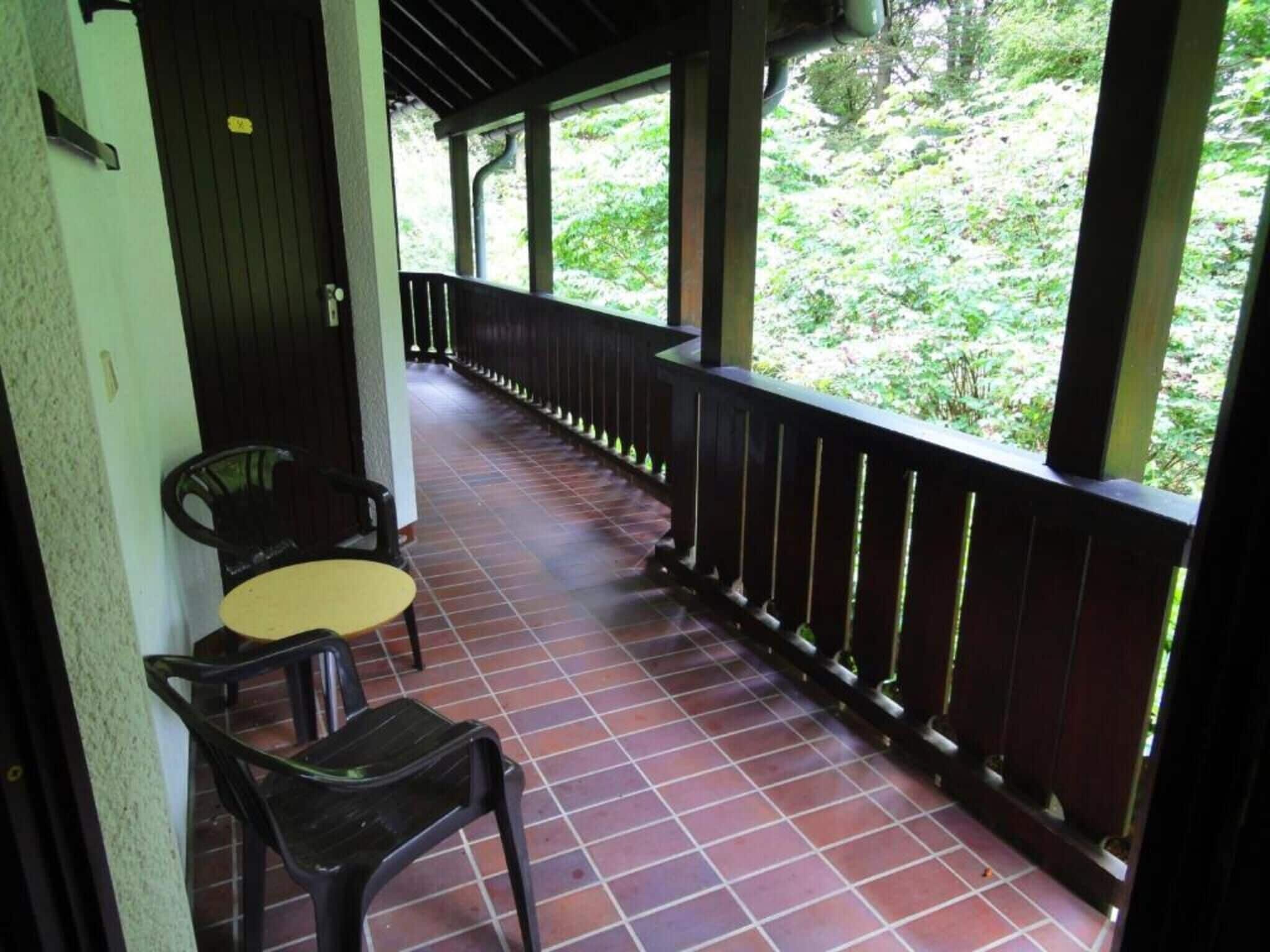 A covered outdoor area with a tiled floor, a wooden railing, and two chairs.