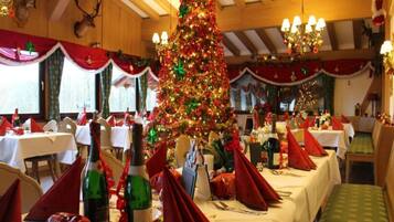 Un comedor con mesas preparadas para una comida, un árbol de Navidad en el centro y un techo alto con vigas de madera.