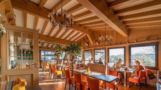 Un restaurant avec des poutres en bois, des chaises orange et de grandes fenêtres.