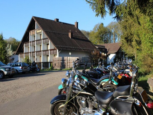 A building with a sloped roof, parked motorcycles, and a car in front. - Belvilla Heiderhof in Rheinischen Westerwald (Obersteinebach)