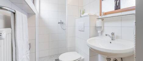 Baño con inodoro blanco, lavamanos y ducha.