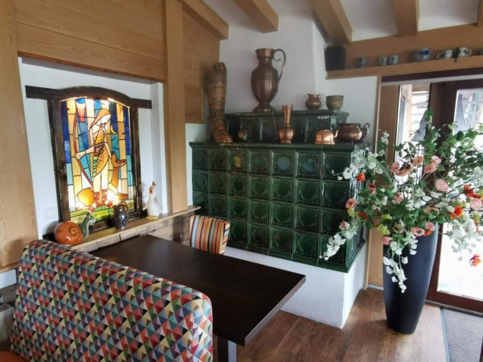 A dining area with a table, chairs, a colorful geometric-patterned bench, a stained glass window, and a green tiled backsplash with decorative items.
