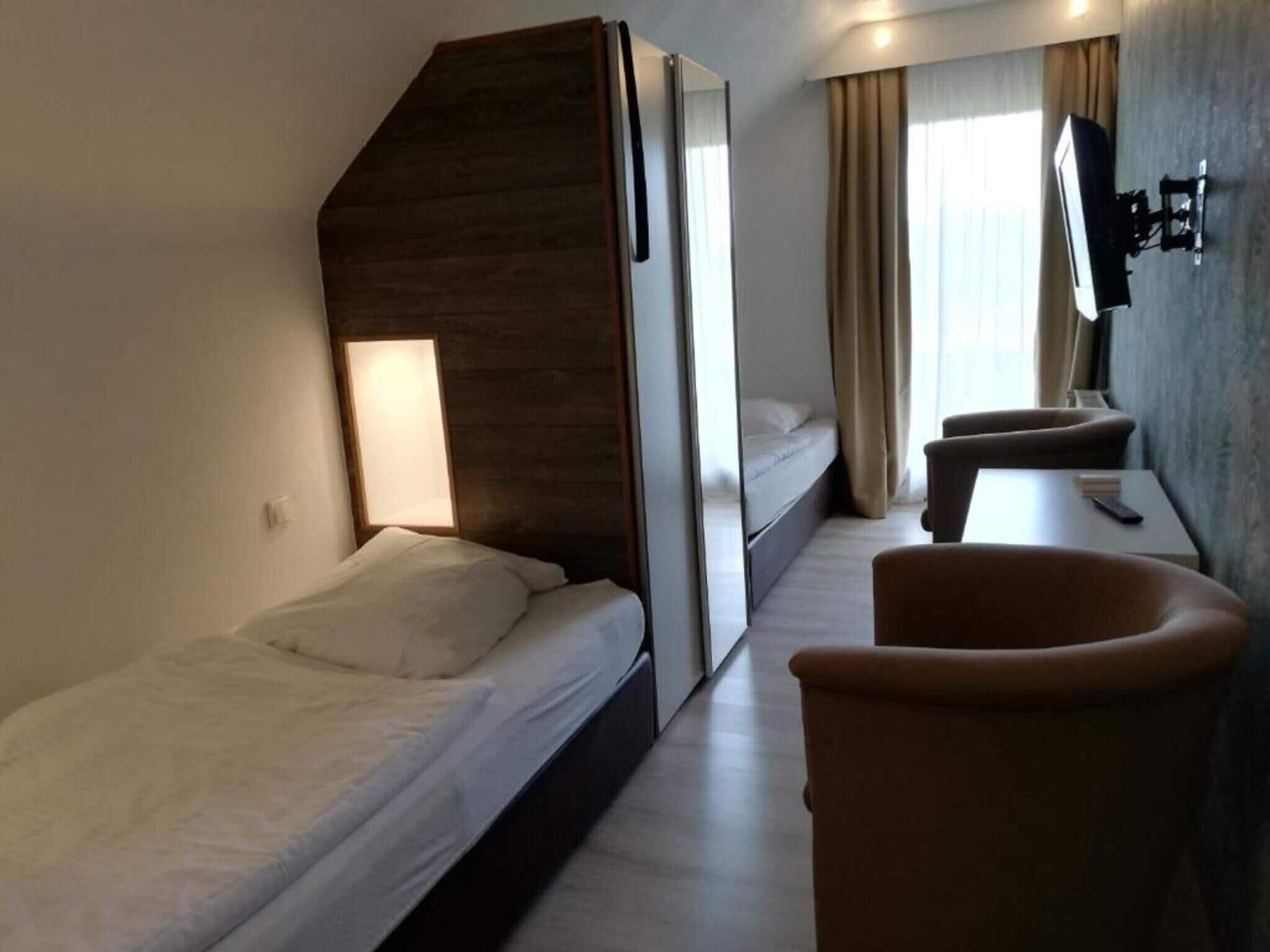 A compact hotel room with a bed, a desk, a chair, a TV, and a window with curtains.
