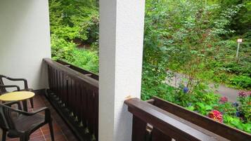 A balcony with a view of a lush garden, a wooden railing, and a small table and chair.