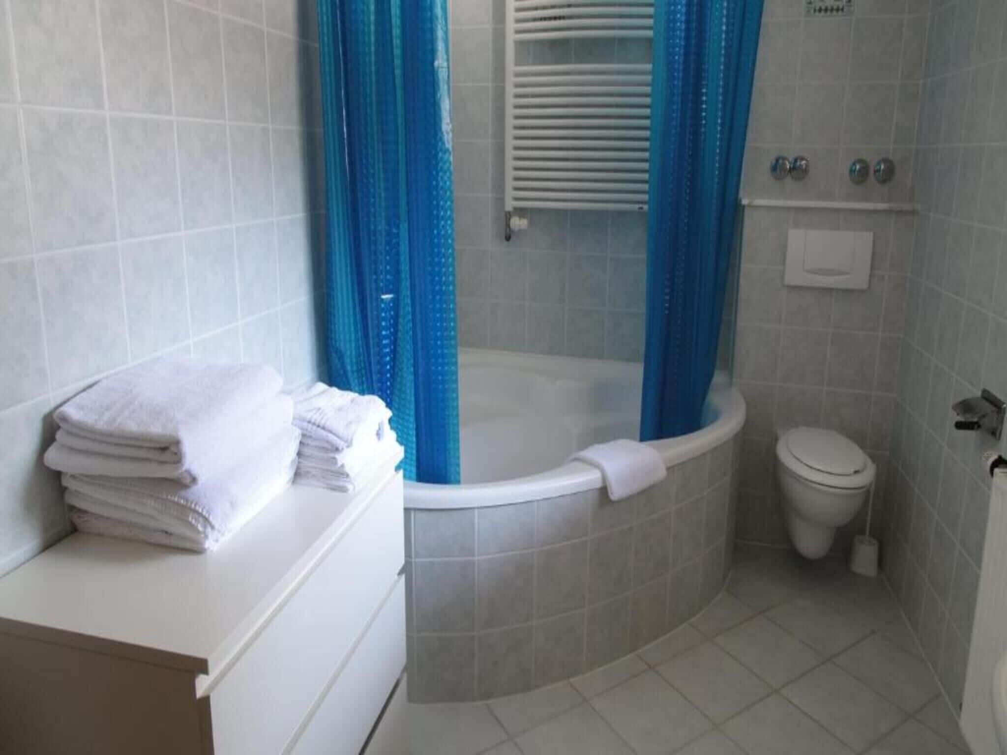 A bathroom with a bathtub, toilet, and a stack of white towels on a counter.