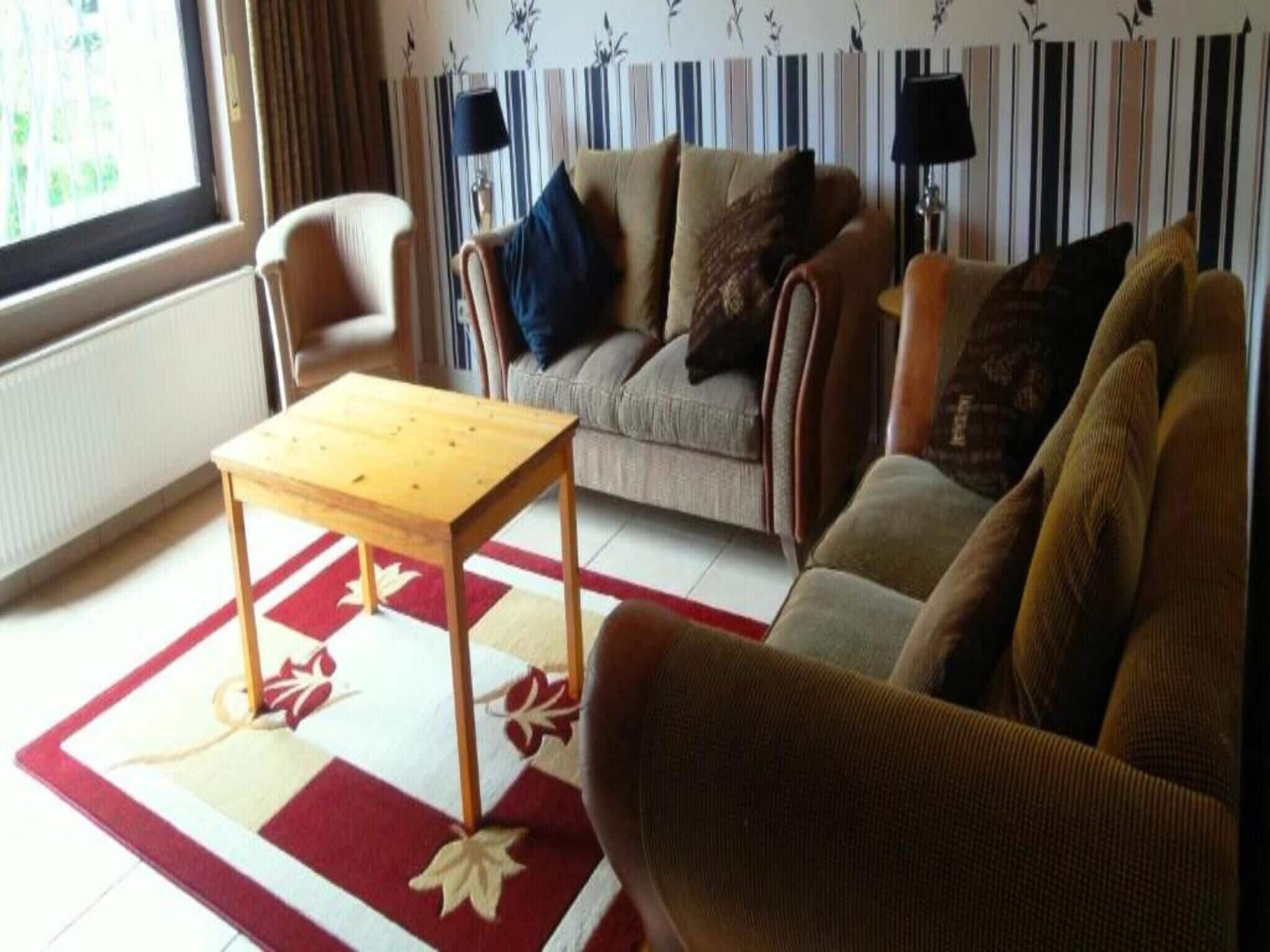 Ein Wohnzimmer mit einer Couch, Sesseln, einem Holztisch, Streifenmuster-Tapete und einem Fenster mit Jalousien.
