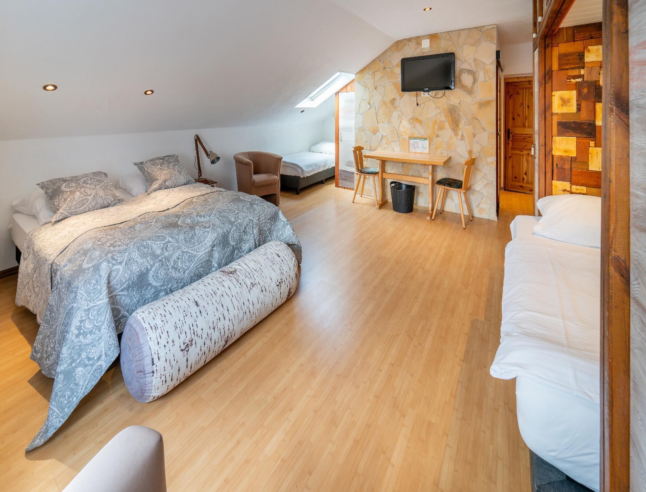 Un dormitorio con cama, escritorio, silla, televisor y pared de piedra.