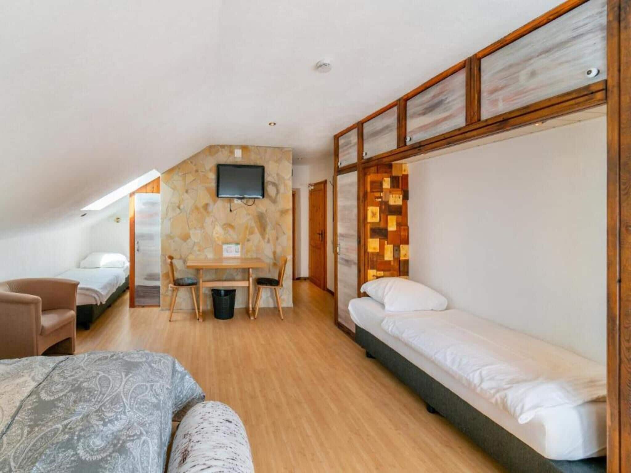 Una habitación compacta con cama, escritorio, sillas, televisor y pared de piedra.