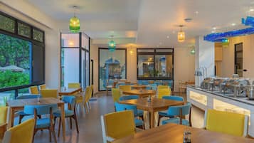 Un comedor moderno con mesas de madera y sillas amarillas, una barra de buffet y ventanas amplias con vistas a la vegetación.