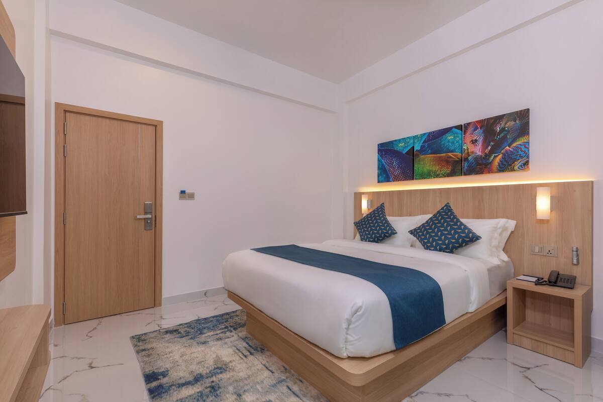A modern bedroom with a bed, wooden headboard, bedside table, and artwork on the wall.