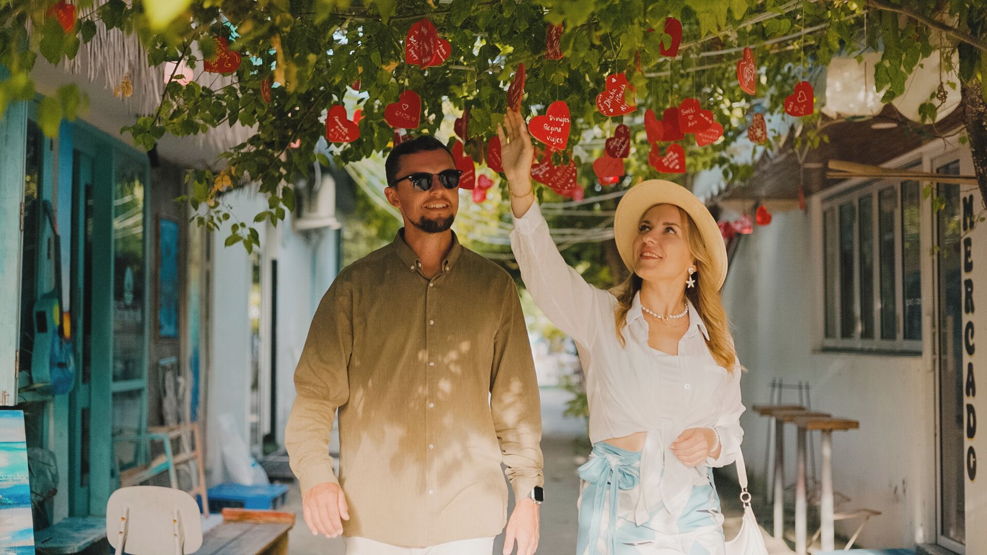 Un hombre y una mujer de pie bajo un árbol con adornos con forma de corazón.