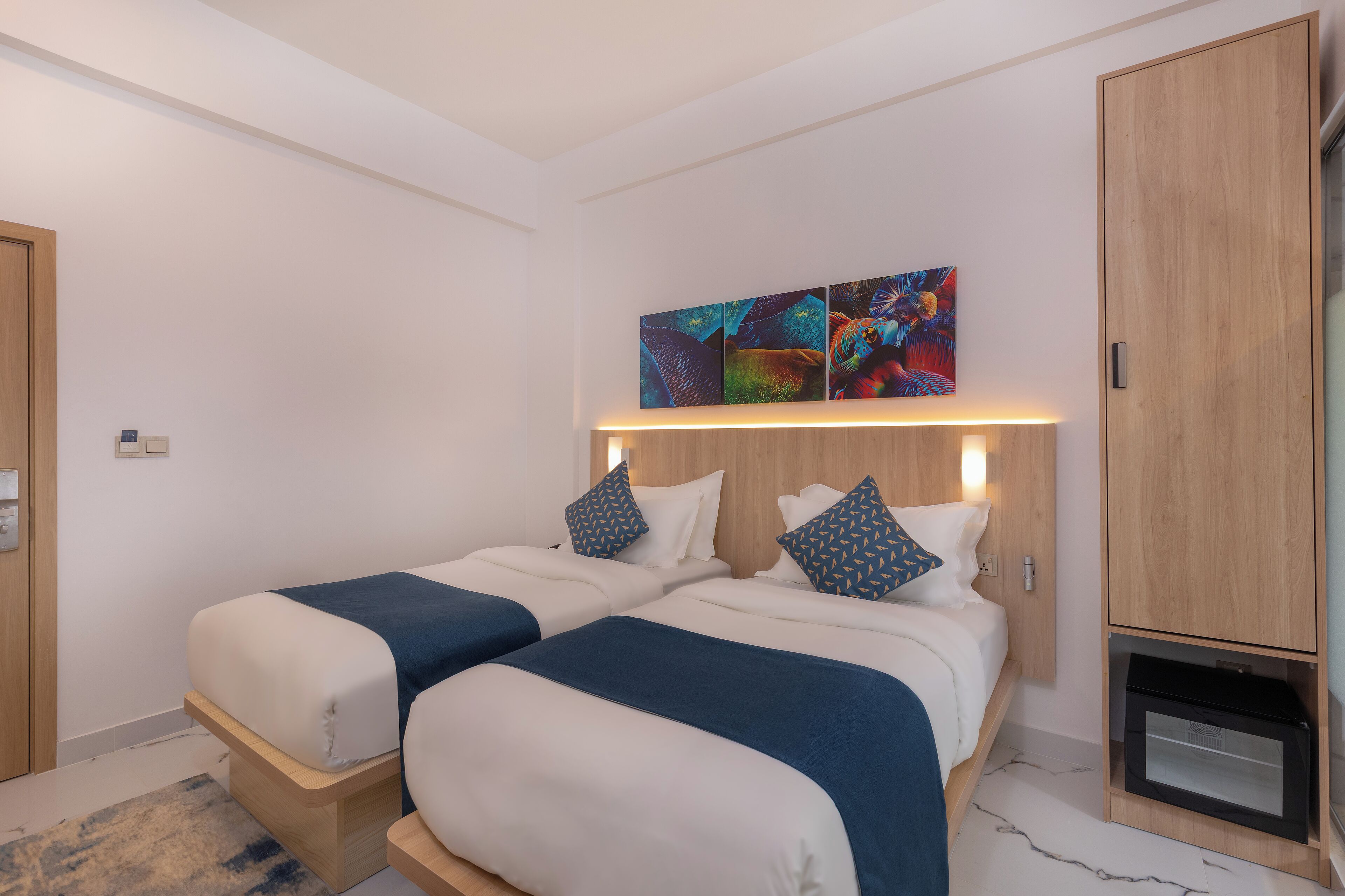 Habitación de hotel moderna con dos camas, un armario de madera y un microondas integrado.