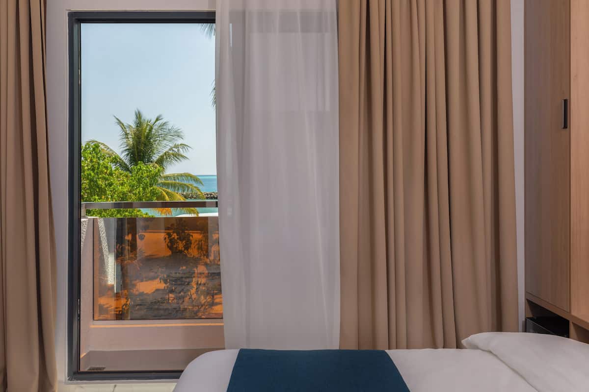 A hotel room with a large window, a bed, and a wooden wardrobe.