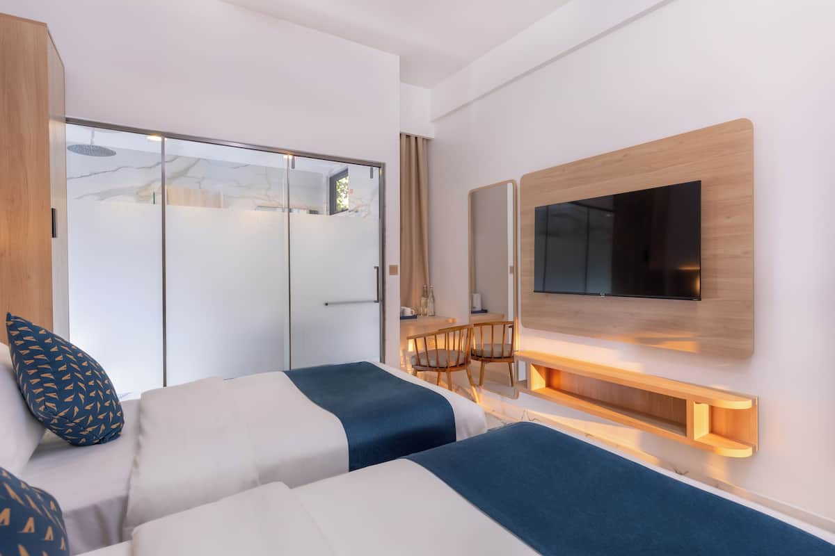 A modern hotel room with two beds, a TV mounted on the wall, a wooden desk, and a sliding glass door.