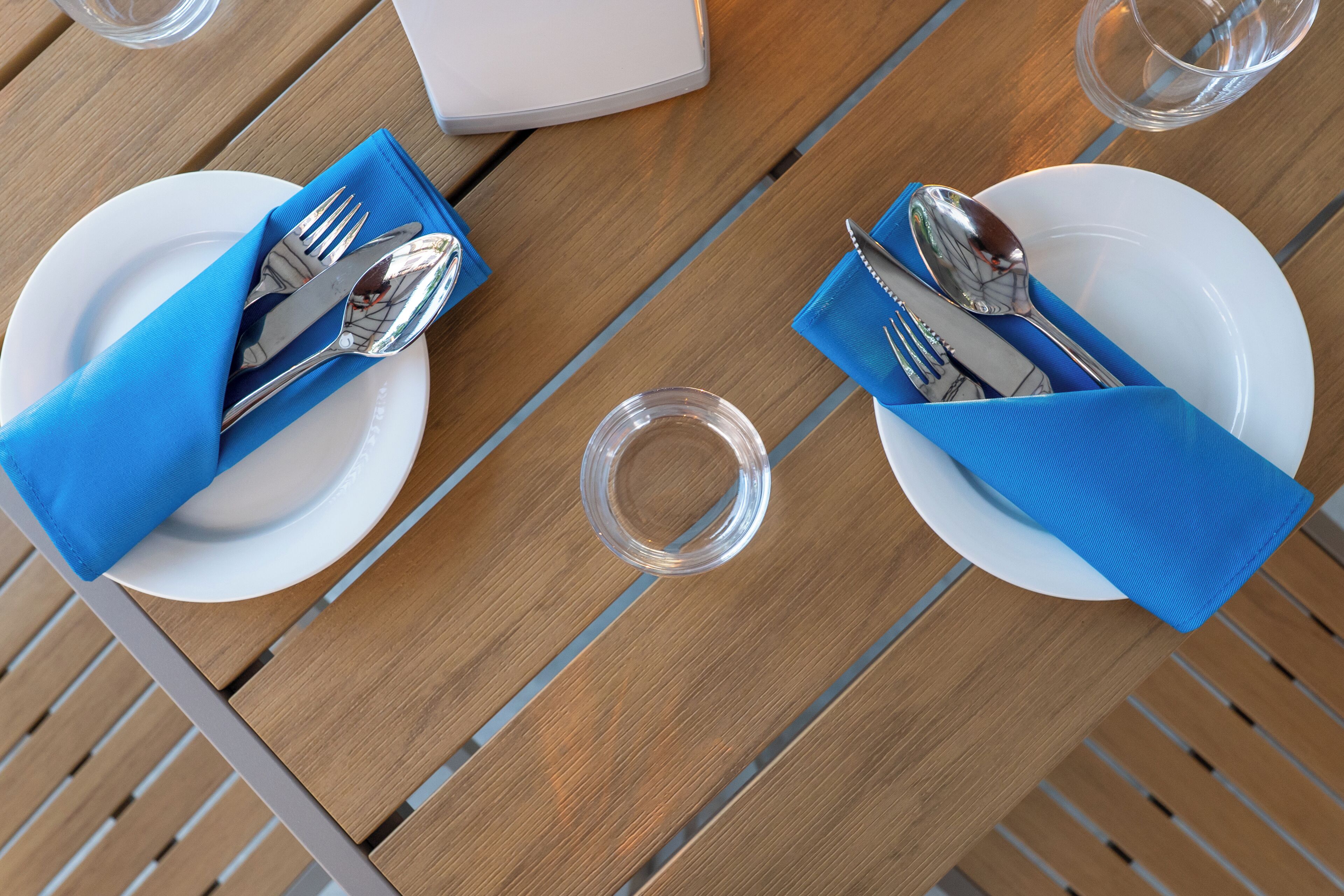 A table set with white plates, blue napkins, and silverware.