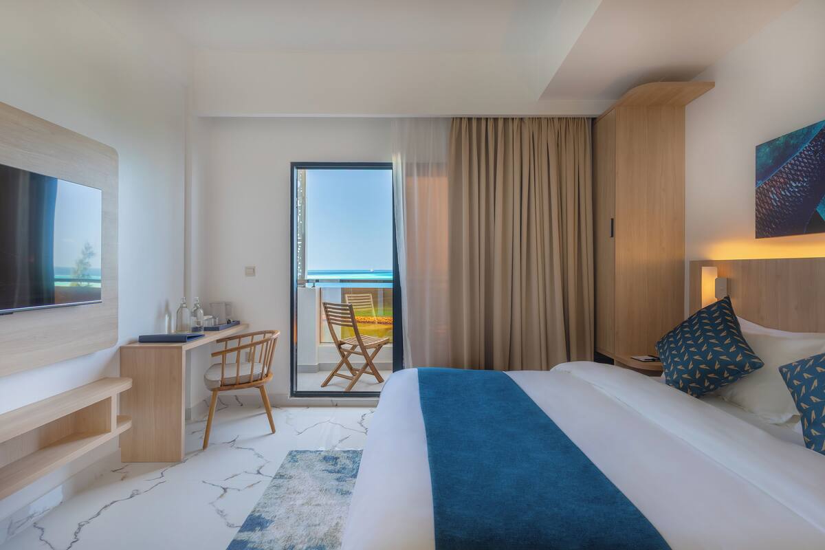 A hotel room with a bed, a desk, a chair, a TV, and a balcony with a view.