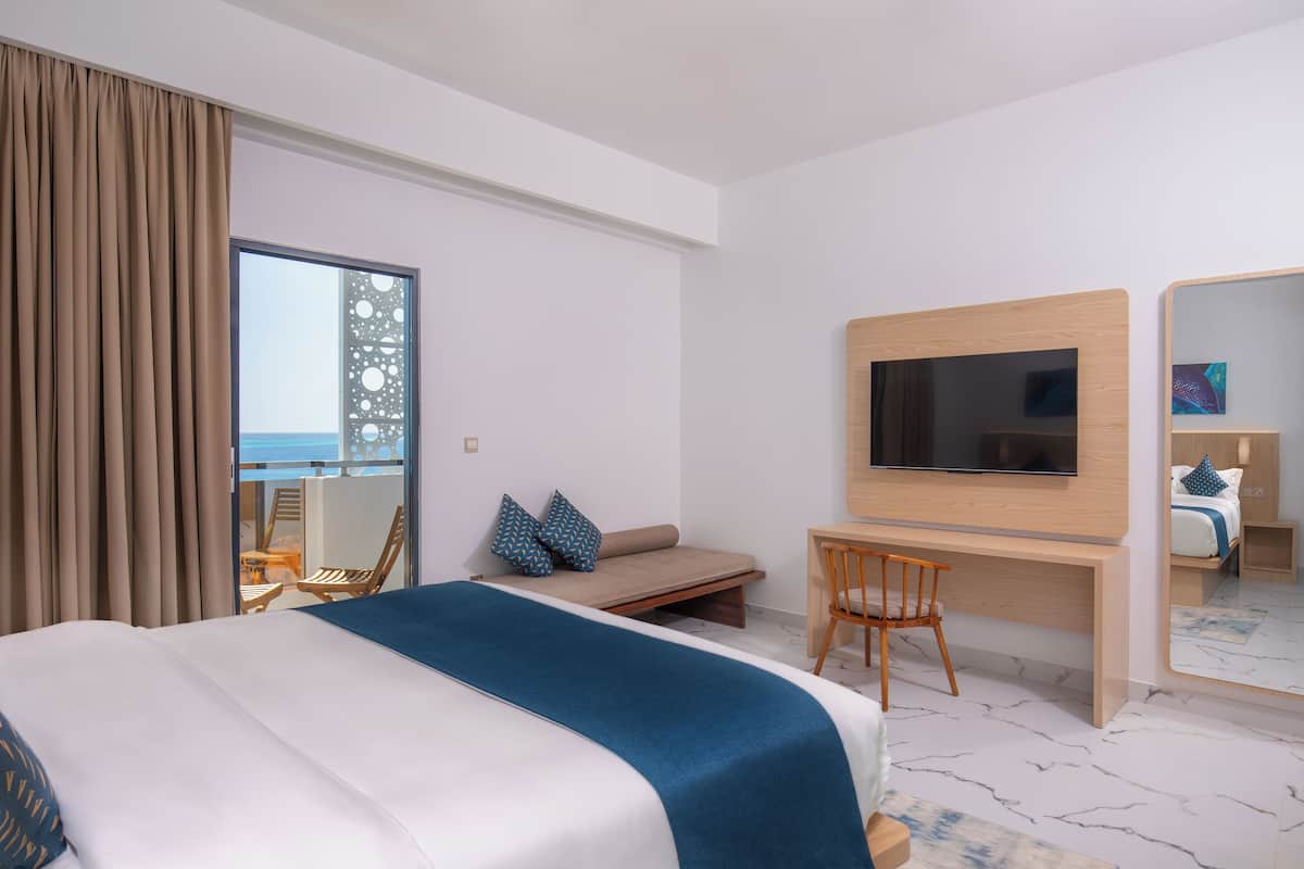 A hotel room with a bed, a desk, a chair, a TV, and a balcony with a view.