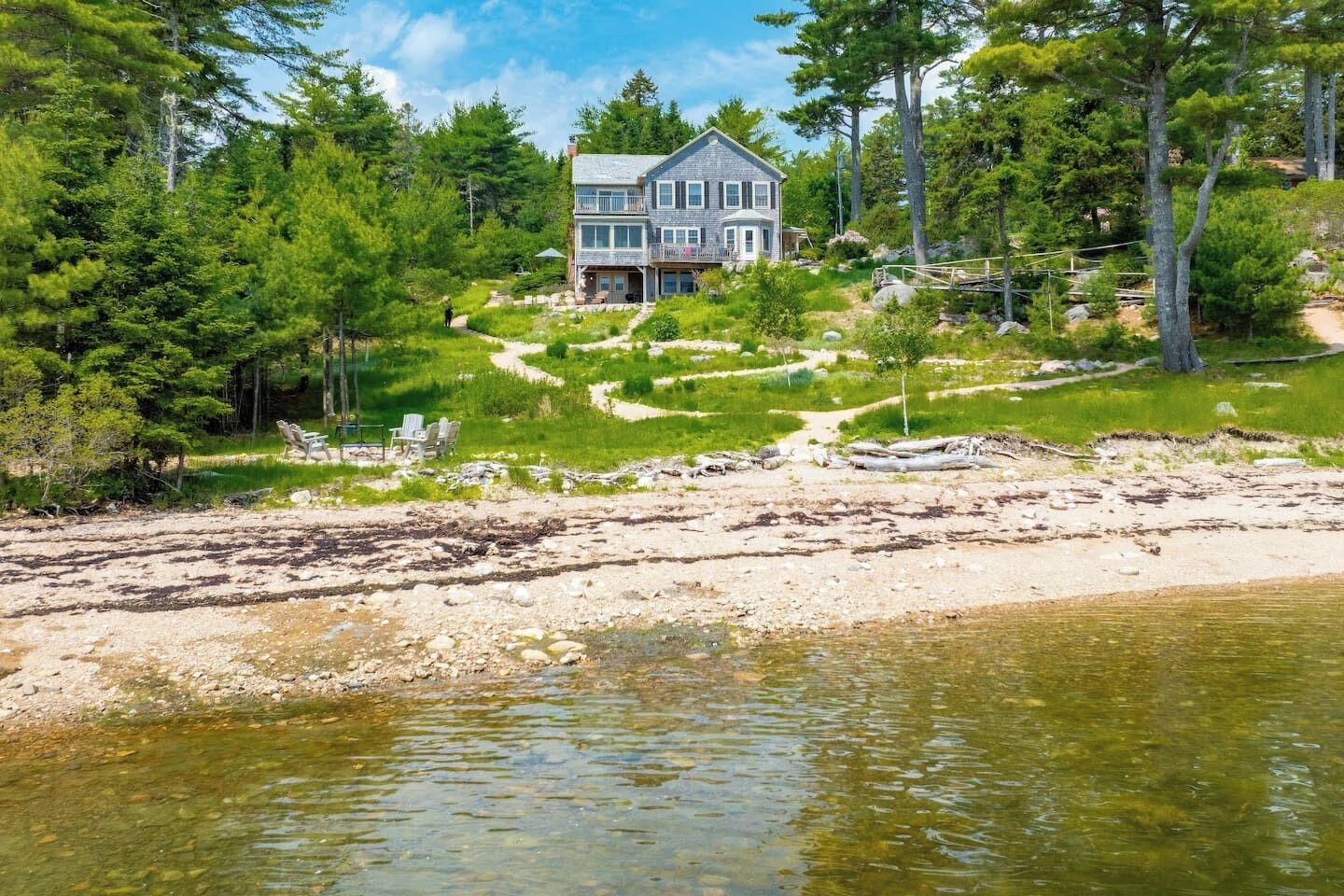 Et toetagers hus med balkon, omgivet af skov og en sandstrand.