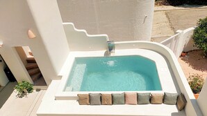 A rectangular hot tub with a built-in seat and a small waterfall feature, surrounded by a white wall and a tiled floor. - Two Bedroom Villa (Porches)