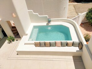 A rectangular hot tub with a built-in seat and a small waterfall feature, surrounded by a white wall and a tiled floor.