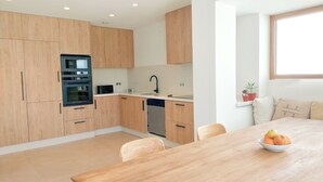 A modern kitchen with wooden cabinets, a built-in oven, and a dishwasher. - Two Bedroom Villa (Porches)
