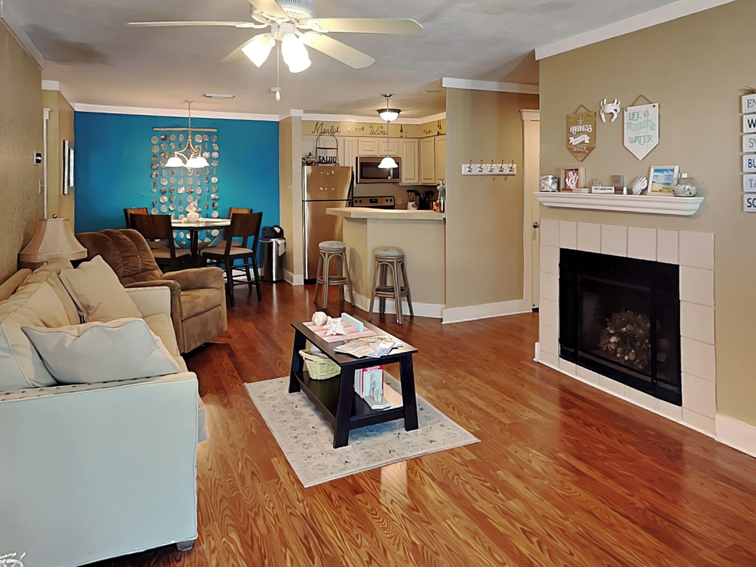 A living room with a sofa, coffee table, and a fireplace. There is a kitchen area with a dining table and chairs.