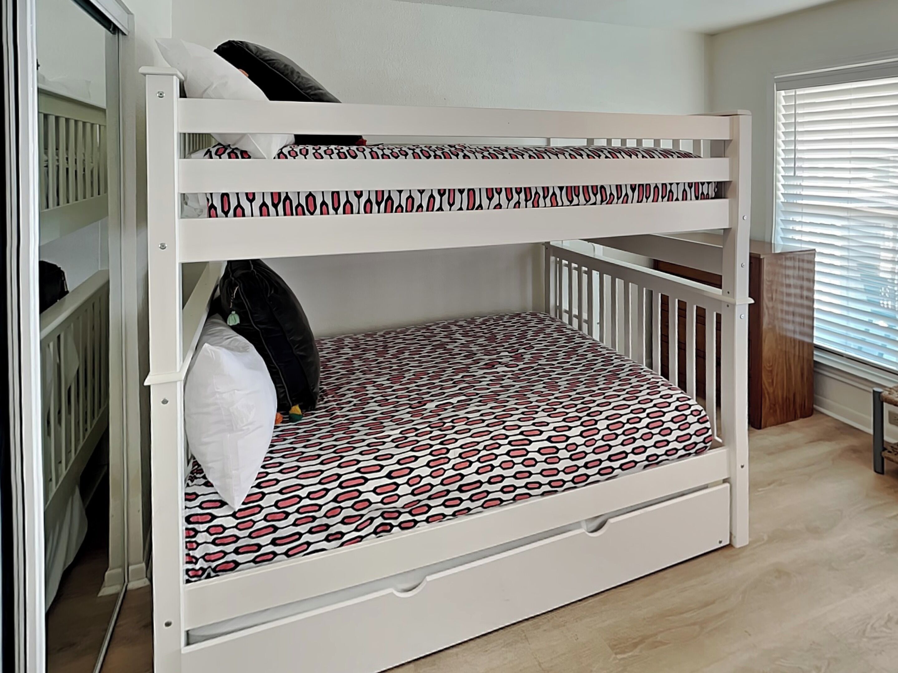 A bunk bed with a patterned mattress, a white crib, and a wooden floor.