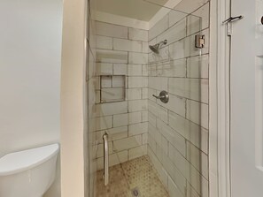 Un baño con paredes de azulejos blancos, una ducha con cabezal de ducha manual y un inodoro.