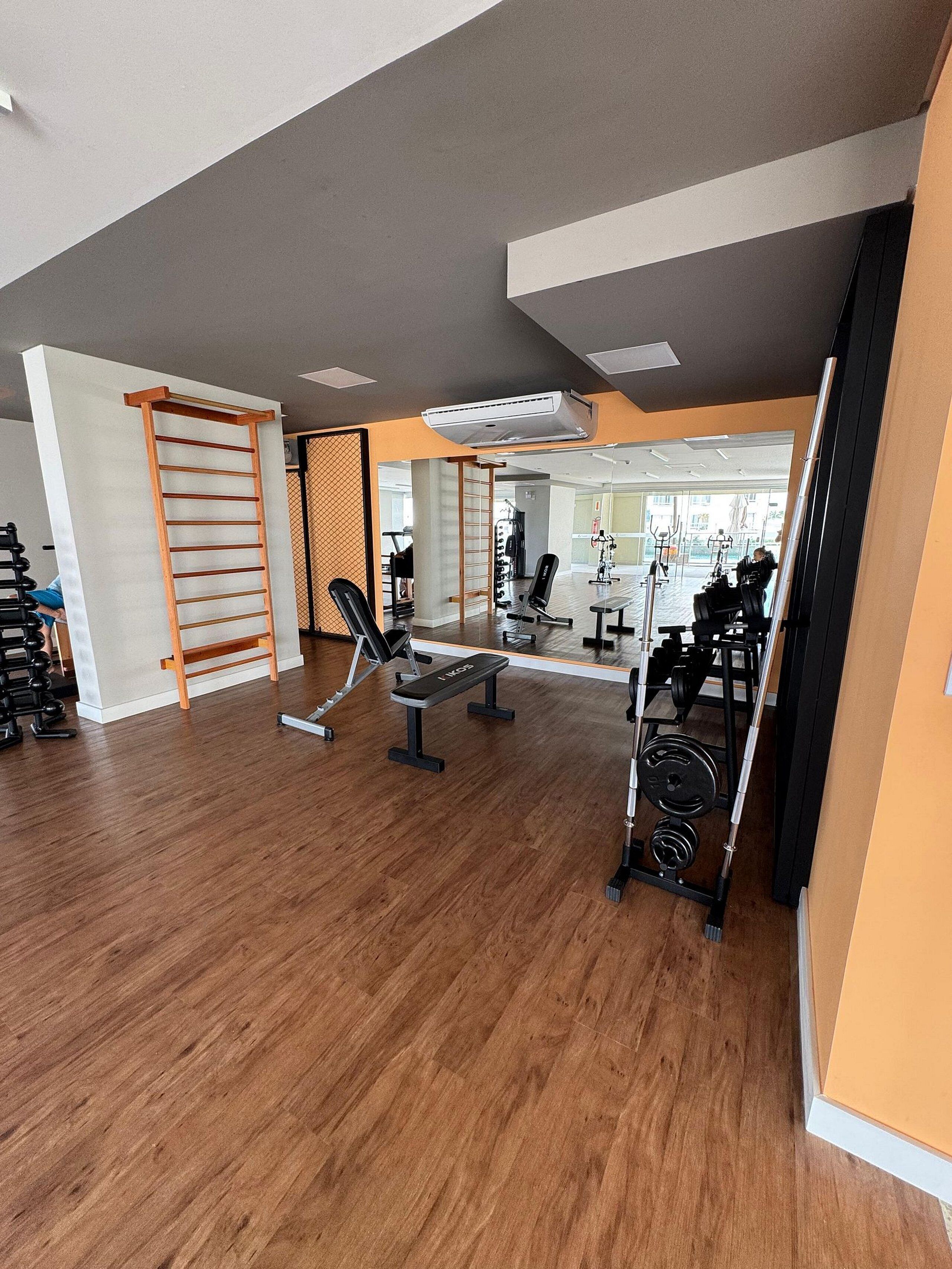 A gym with wooden flooring, exercise equipment, and a mirrored wall.