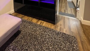 A living room with a TV mounted on a black entertainment unit, a wooden floor, and a grey carpet. - Modern 2BR Near NYC • Free Parking • Quiet Area (Yonkers)