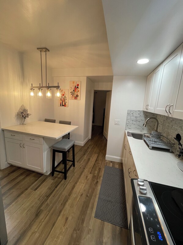 A modern kitchen with white cabinetry, a wooden floor, a central island with seating, and a built-in oven.