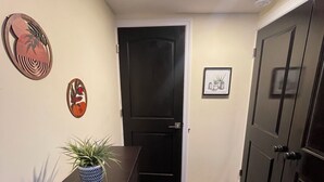 A hallway with a dark brown counter, a potted plant, a framed picture, and a black door. - Modern 2BR Near NYC • Free Parking • Quiet Area (Yonkers)
