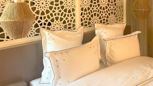 A bedroom with a decorative white partition, a bed with white linens, and two hanging lamps.