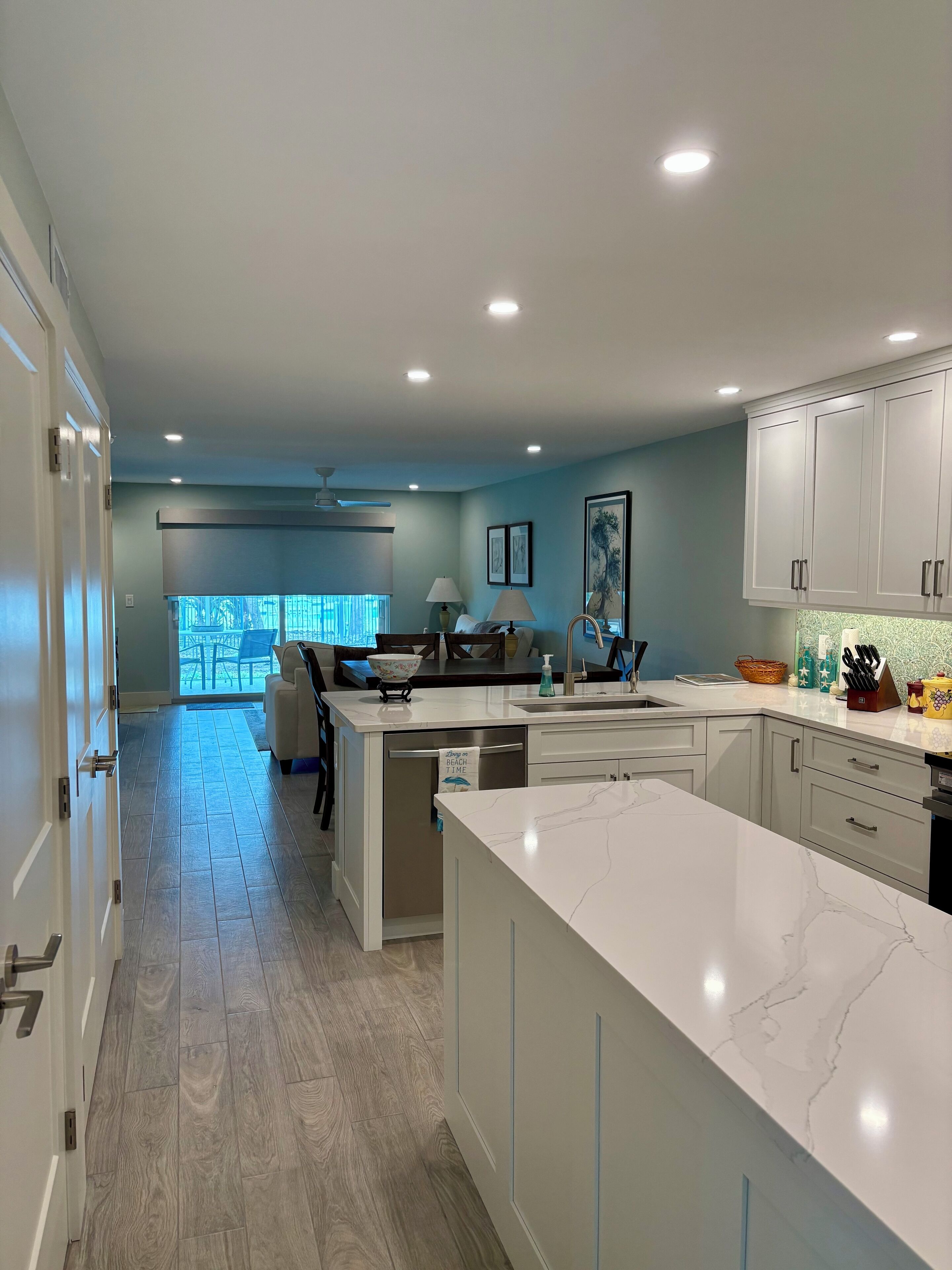 A modern kitchen with a large island, white cabinetry, and a view to the outside.